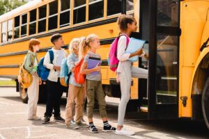 five kids with backpacks and books boarding a yellow school bus