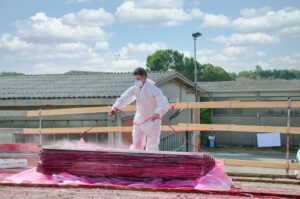 a roofer in white uniform and protective face mask prepares new roofing material outside on a sunny day