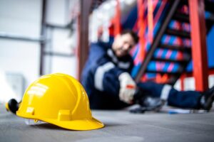 injured worker in the back holding his leg while his construction hat is on the floor